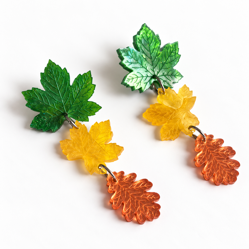 Pendientes Danza de Otoño de Sergi Bastian con tres hojas verdes, amarillas y naranja espejo sobre fondo blanco.