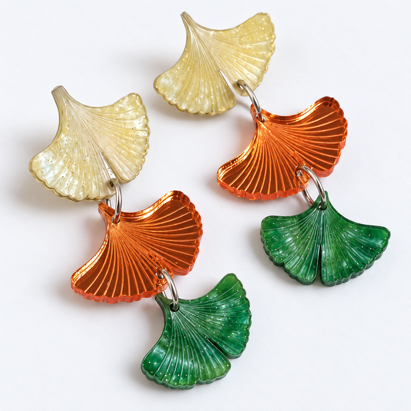 Pendientes Ginkgo de Otoño de Sergi Bastian: tres hojas articuladas en nácar amarillo claro, espejo naranja y verde con aguas y glitter fino.