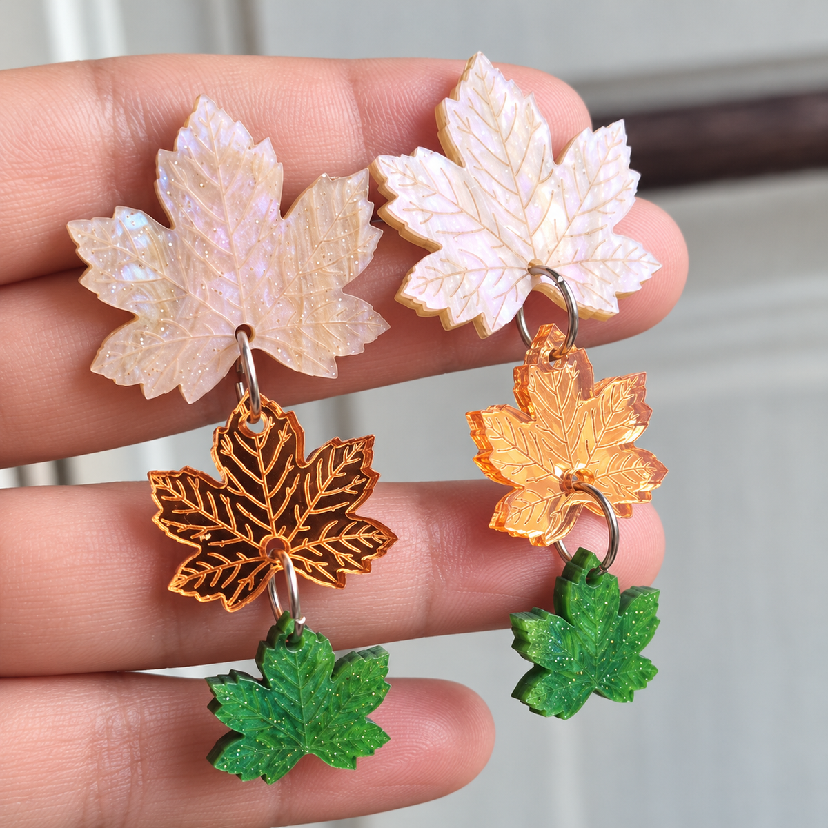 Detalle de los pendientes Hechizo de Otoño en la mano, con hojas blancas nacaradas, reflejos dorados rosados y hojas verdes con aguas.