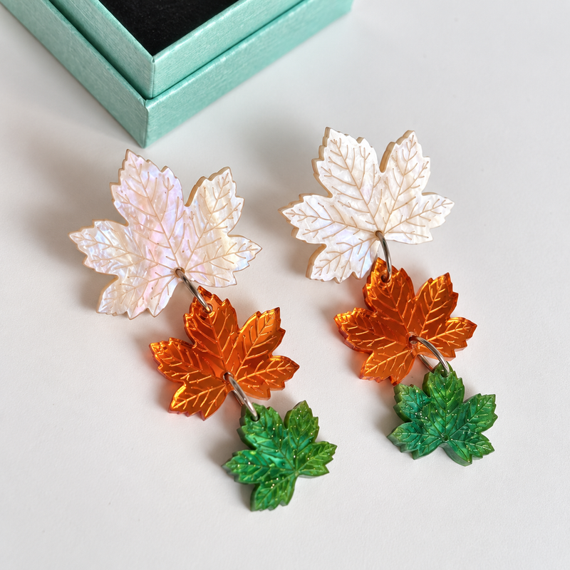 Pendientes Hechizo de Otoño de Sergi Bastian: tres hojas articuladas en blanco nacarado, espejo dorado rosado y verde con aguas y glitter fino.