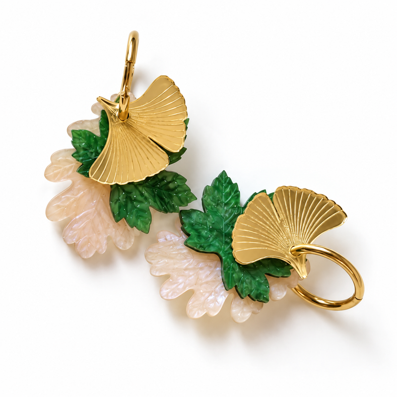 Pendientes Luz de Ginkgo de Sergi Bastian: tres hojas en espejo dorado, verde con aguas y nácar lila claro, sobre fondo blanco.