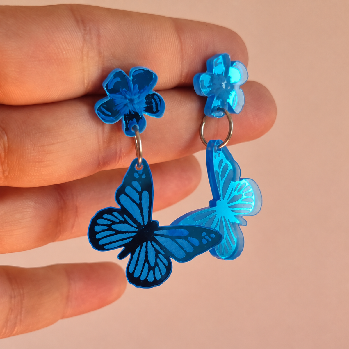 Pendientes Mariposa turquesa espejo sostenidos en la mano, referencia de tamaño en formato cuadrado