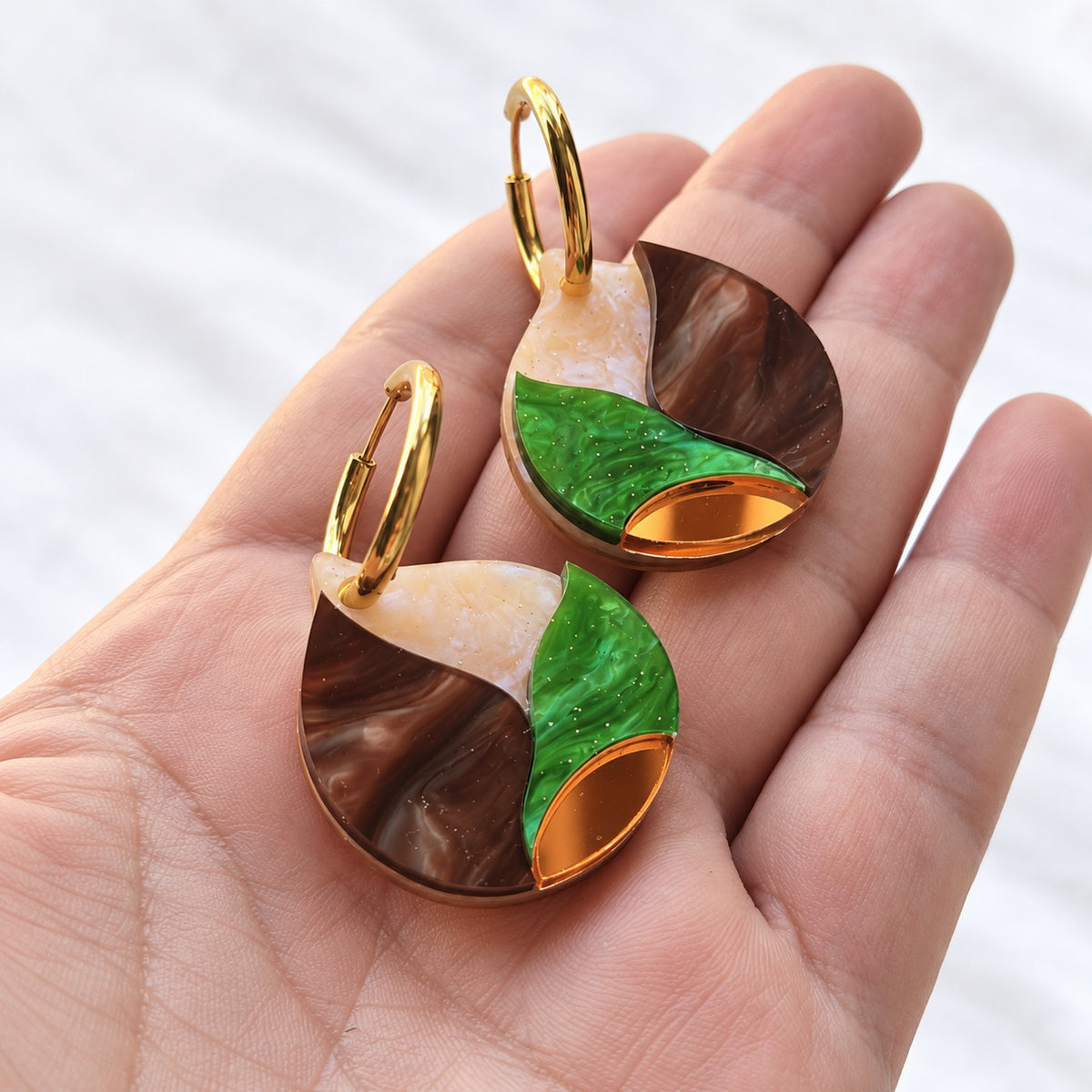 Par de pendientes Nácar de Otoño sobre la mano, detalle del nácar, glitter y espejo cobrizo.