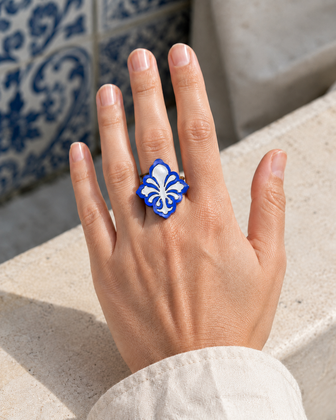 Anillo Alma de Oporto de Sergi Bastian, de 3 cm de alto, en azul y blanco nacarados, puesto en una mano ante azulejos portugueses.
