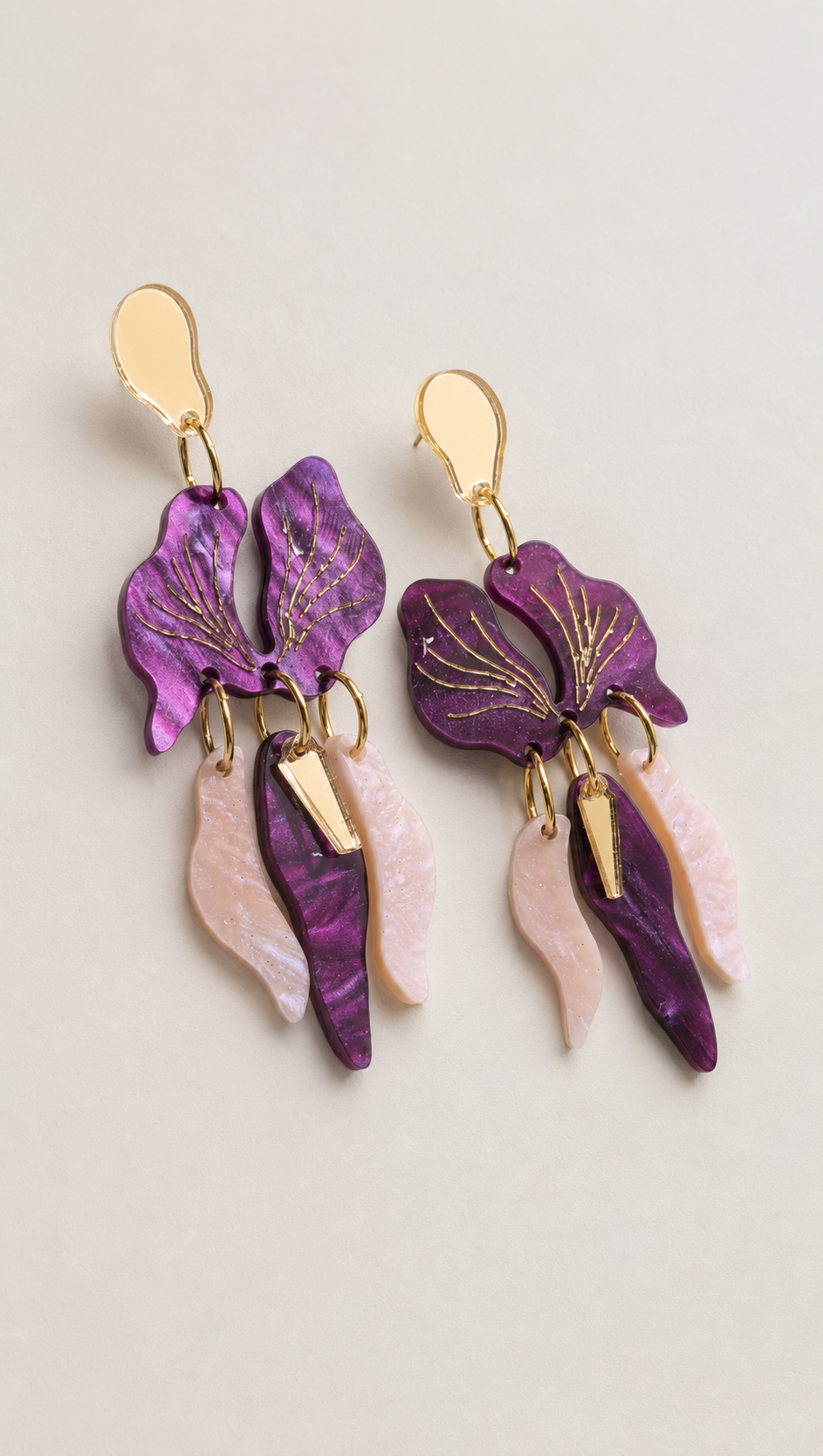 Pendientes Orquídea de metacrilato lila nacarado, rosa glitter nebulosa y espejo dorado, sobre fondo neutro.